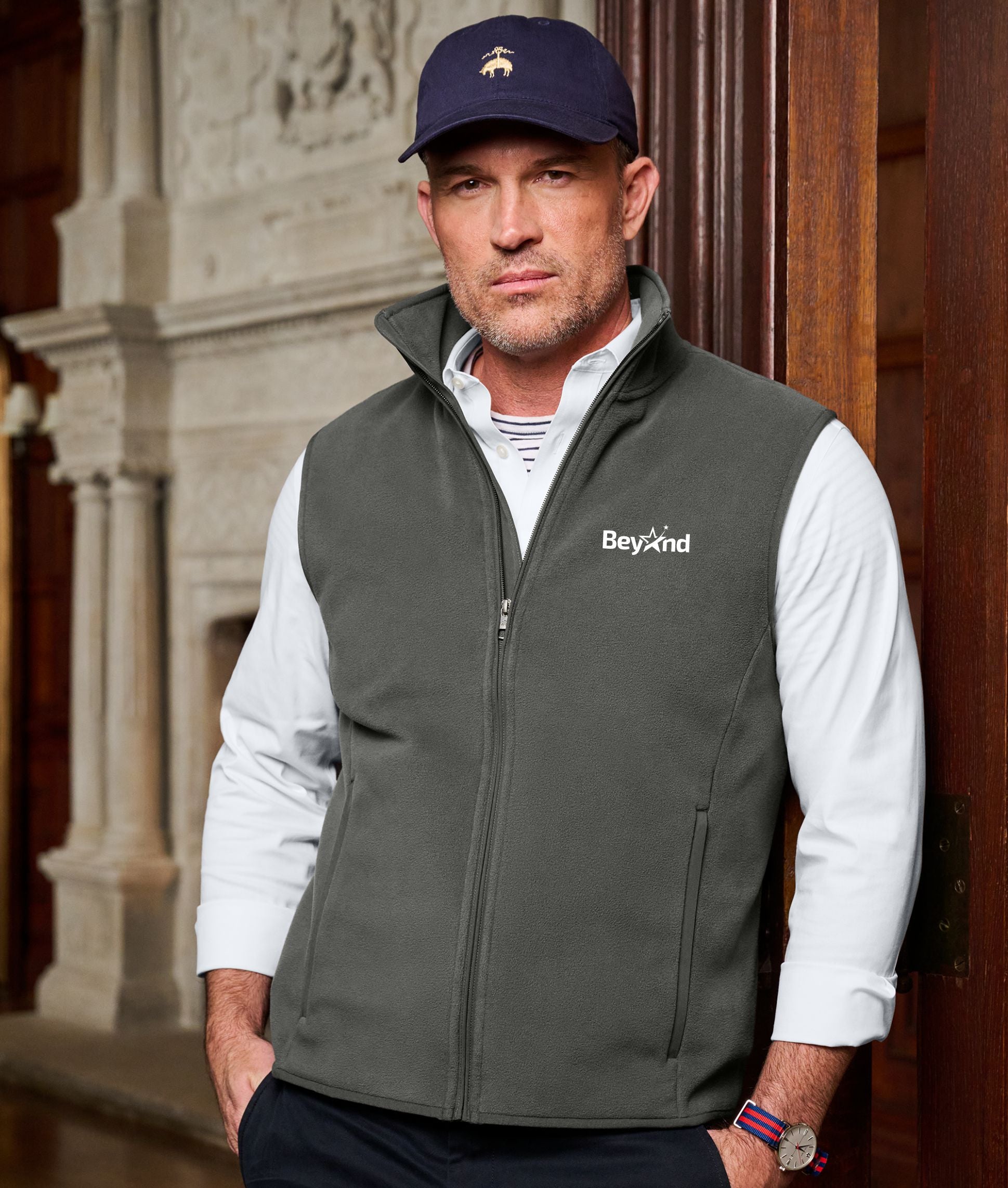 A man in work attire wearing a branded sweater vest and branded hat
